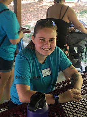 A person smiling at a picnic table outdoors, wearing a turquoise shirt with the name tag "Allison."