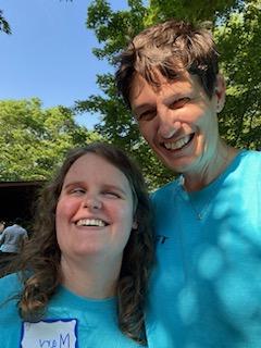 Two people smiling outdoors on a sunny day, wearing blue shirts.